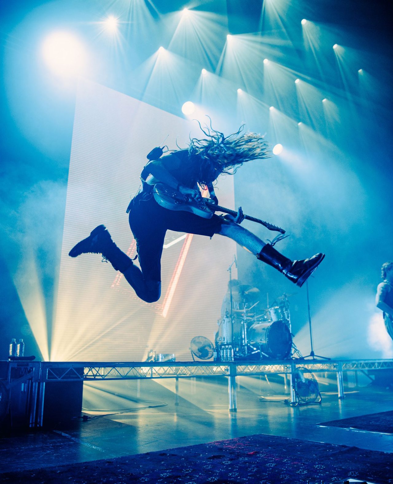 Guitarist jumps beneath blue-white stage beams at a Spacey Jane show.