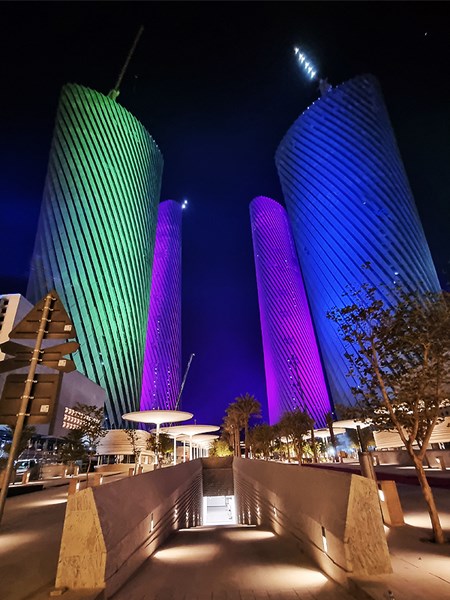 Green, blue and purple lighting across the curved Lusail Plaza Towers at night.
