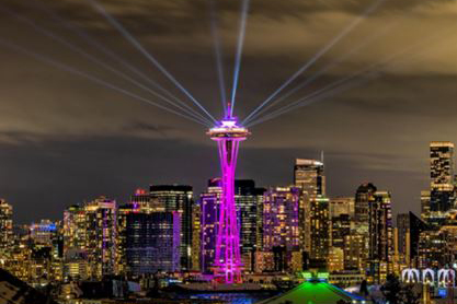 Searchlight beams radiate above the illuminated Space Needle at night.