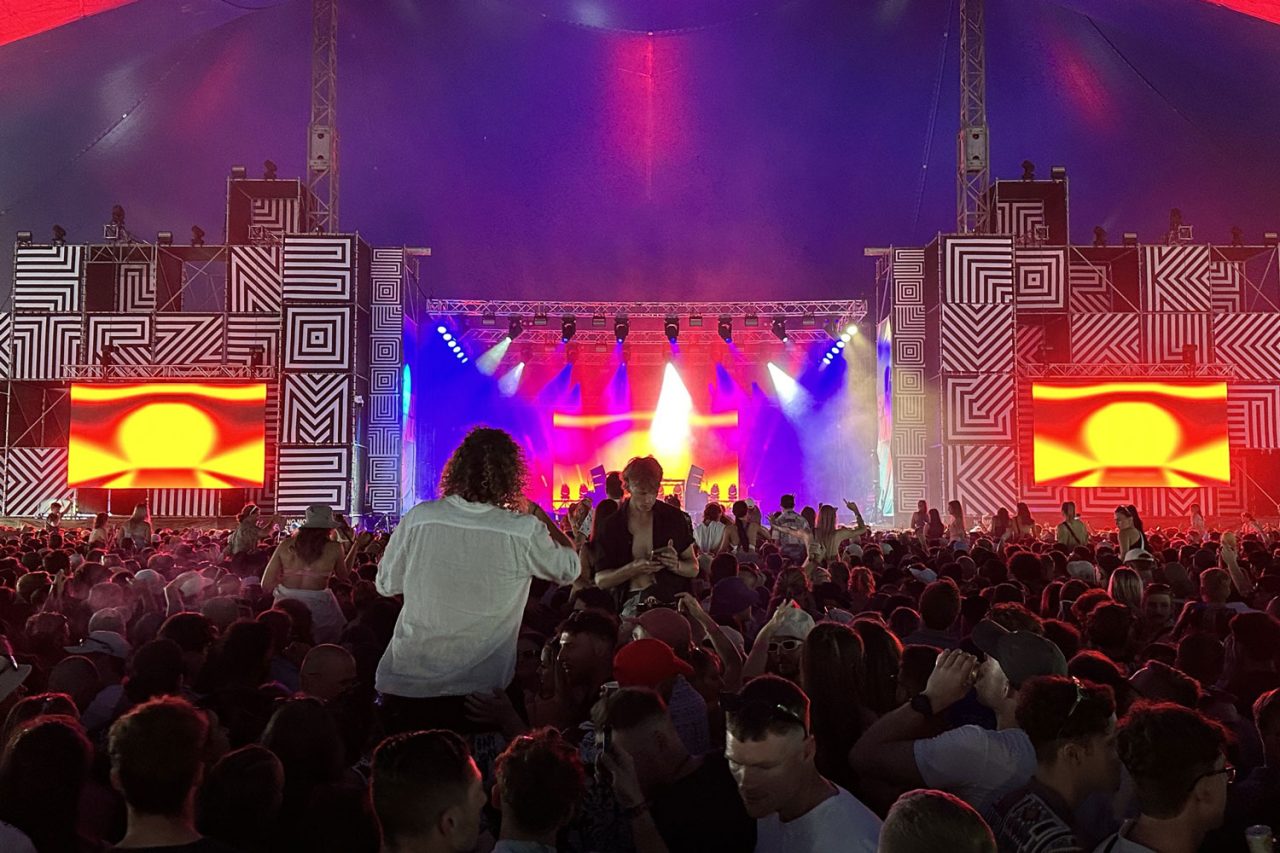 Crowd facing a colourful stage and side screens at Spilt Milk.