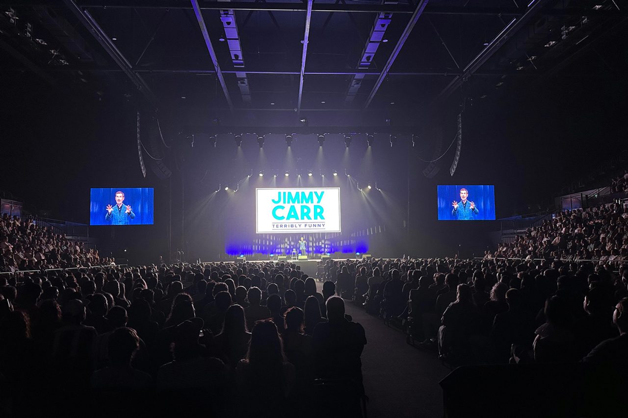 Wide view across the audience towards the three screens at Jimmy Carr's Terribly Funny show.