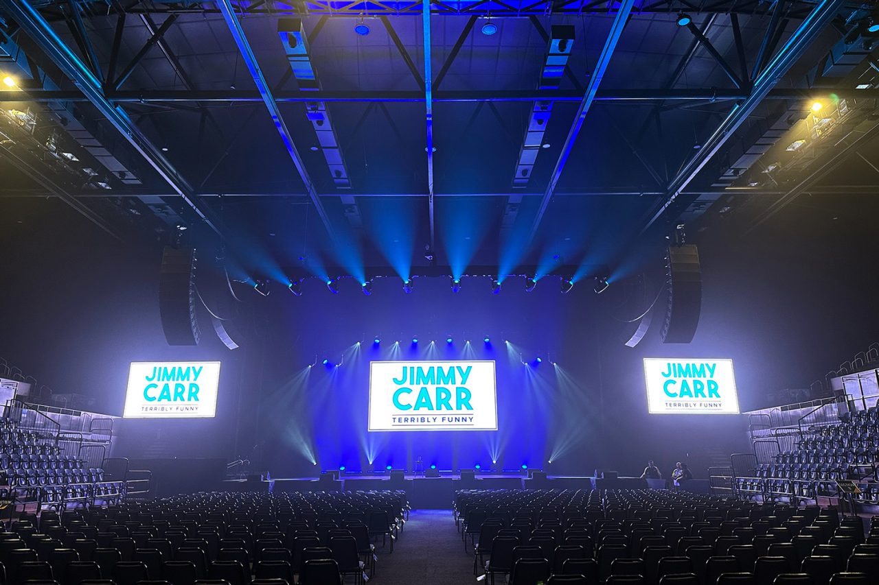 Blue beams above three Terribly Funny screens in the arena before the show.