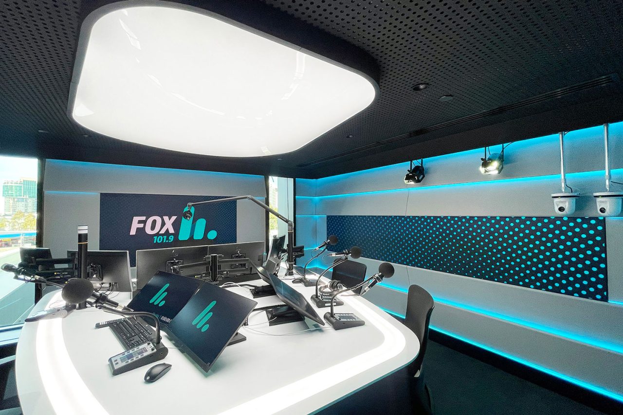 Broadcast desk beneath a large ceiling light in the Fox studio at Southern Cross Austereo.