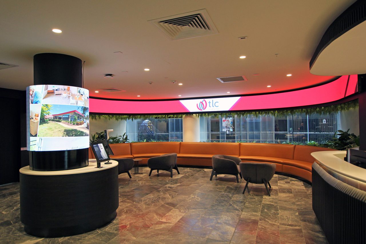 Red imagery on a curved ribbon display above seating at TLC Aged Care reception.