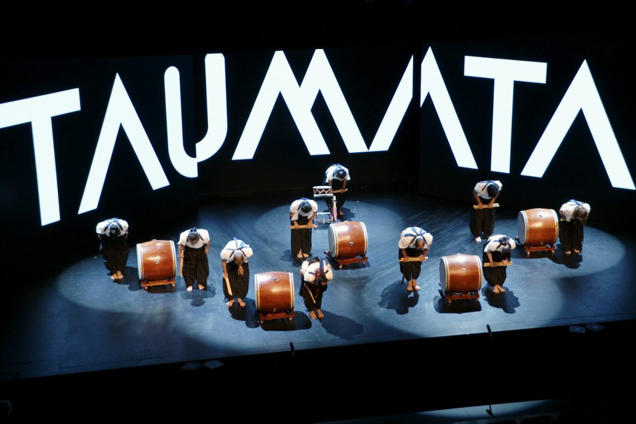 Drums arranged on stage in front of large Taumata lettering.