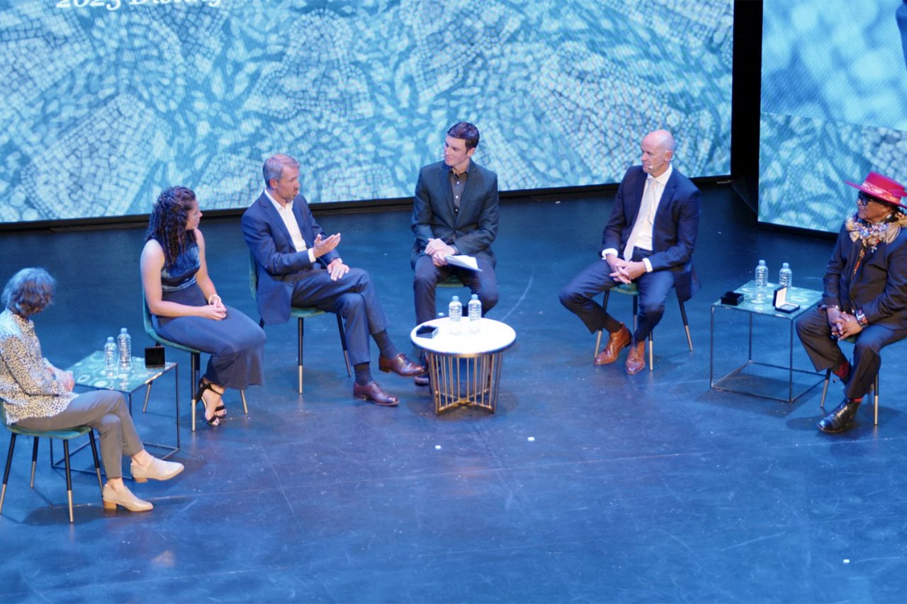 Seated panel discussion in front of blue imagery on the Taumata stage.