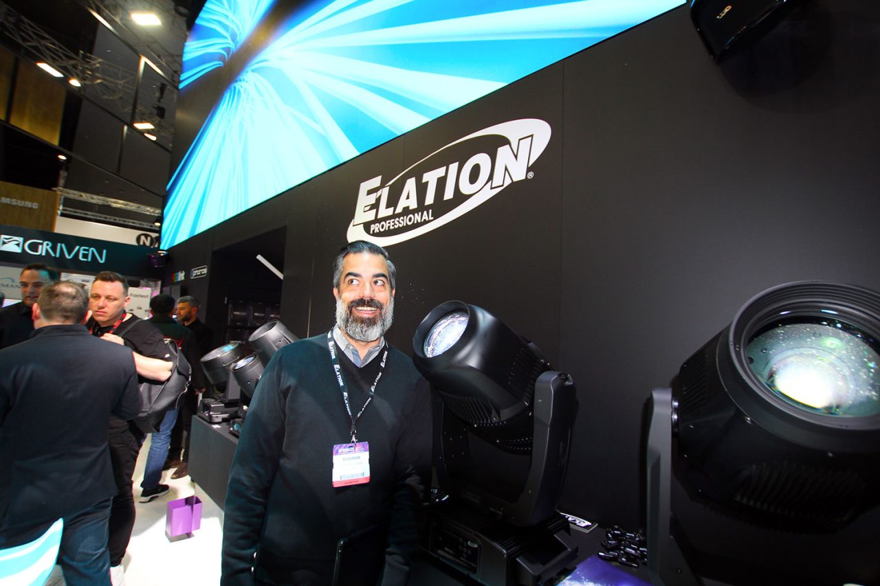 Representative beside Elation moving-head fixtures at an exhibition stand.