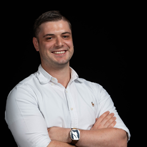 Rod standing with folded arms in a white shirt against a dark background.
