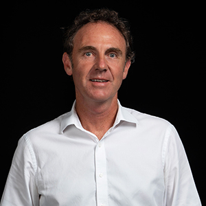 Tony wearing a white shirt against a dark background.