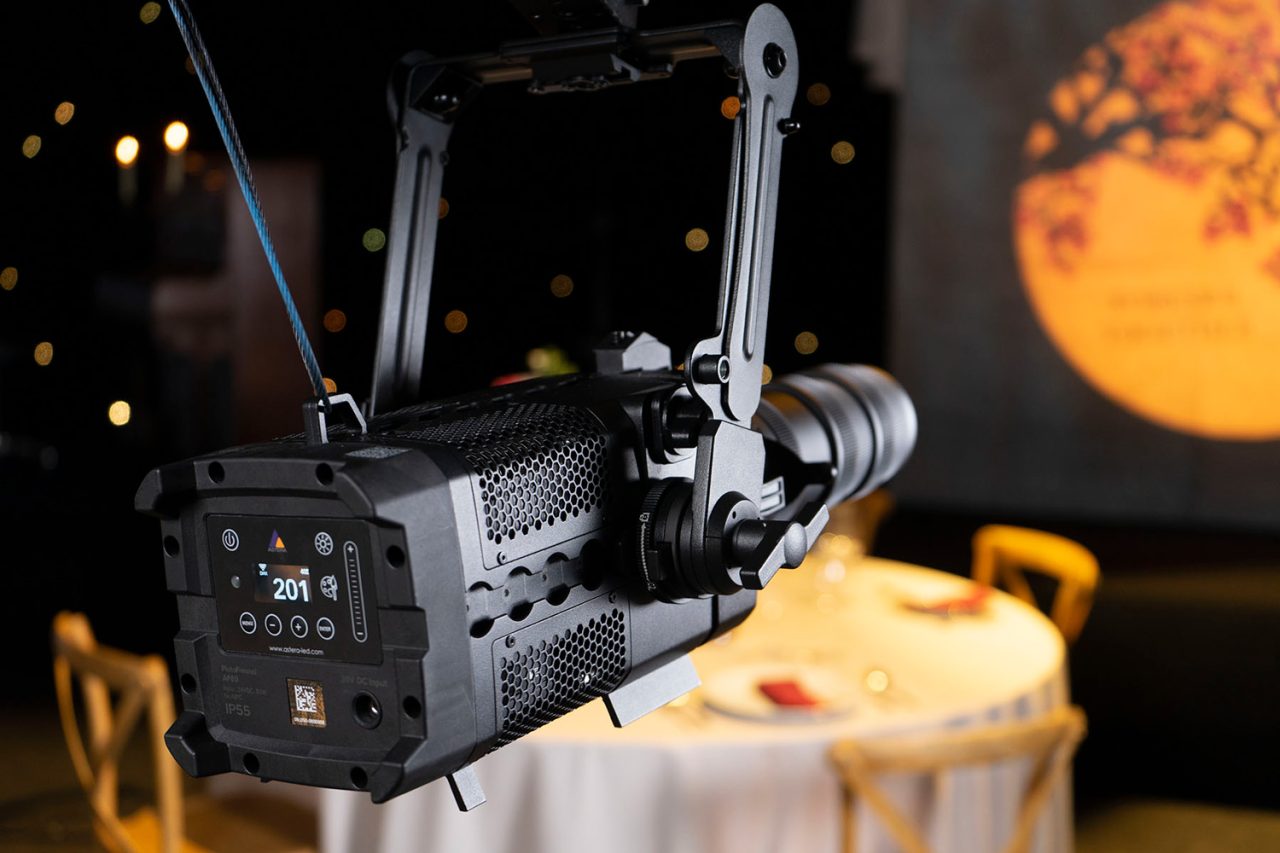 Rear controls of a rigged Astera projector with an orange gobo pattern on the wall.