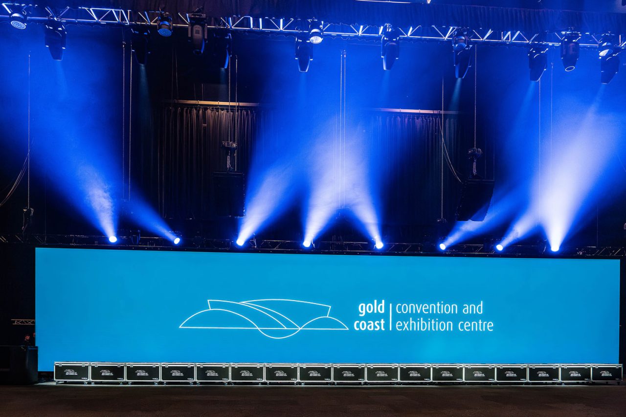 GCCEC branding on a blue panoramic LED wall beneath stage beams.