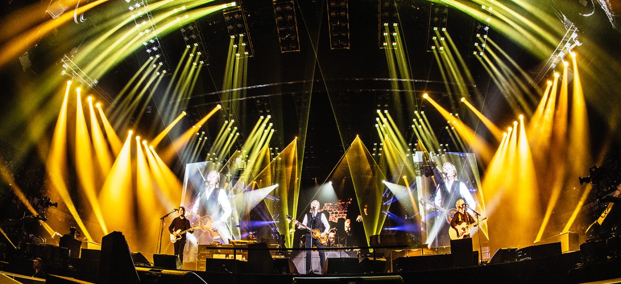 Band performing beneath gold and white beams on Paul McCartney's Get Back tour.