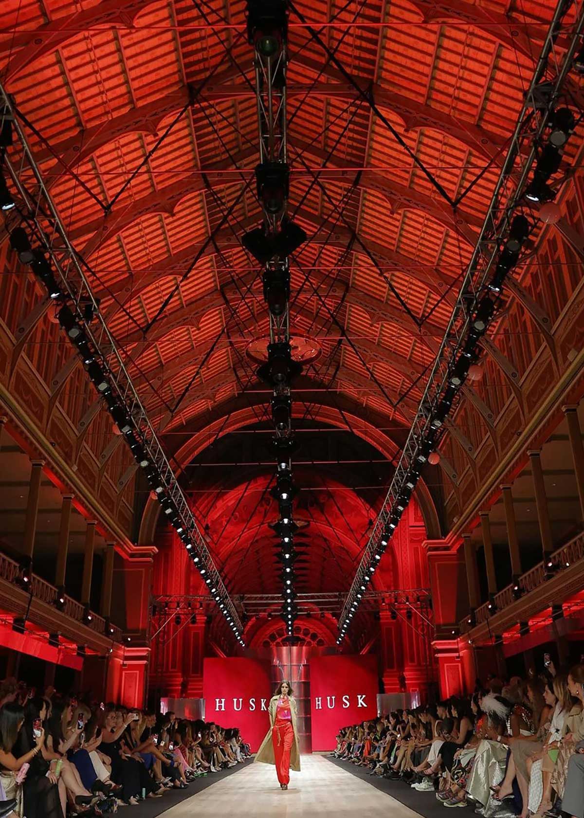 Long runway inside the Royal Exhibition Building, with a red-lit roof and spectators seated along both sides.