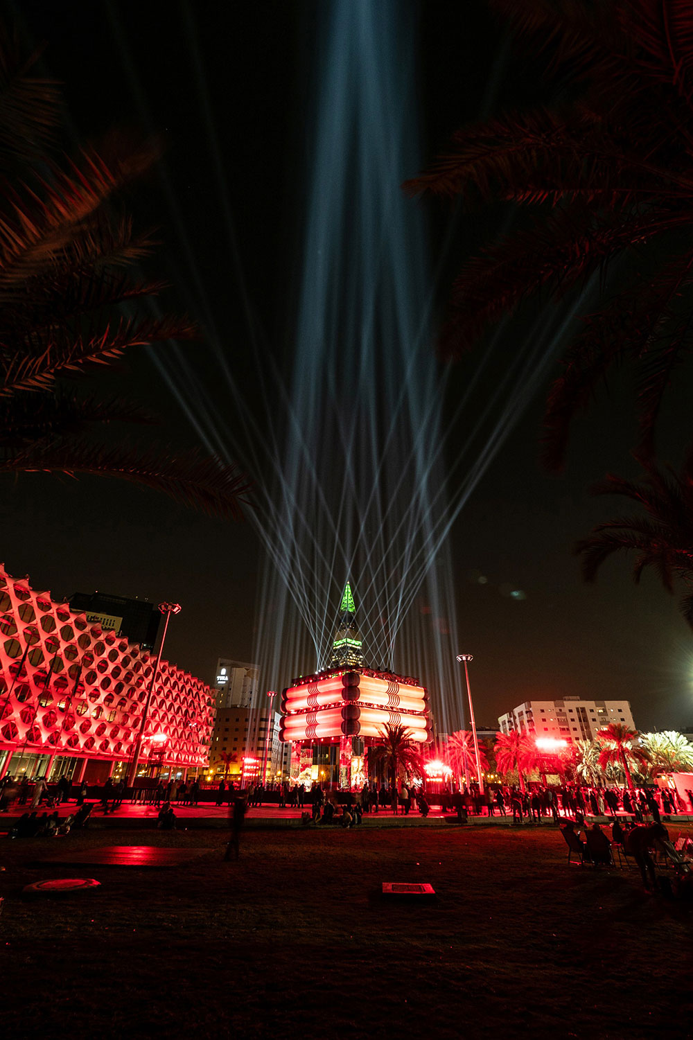 Wide night view of the agal-inspired installation with blue beams rising into the sky.