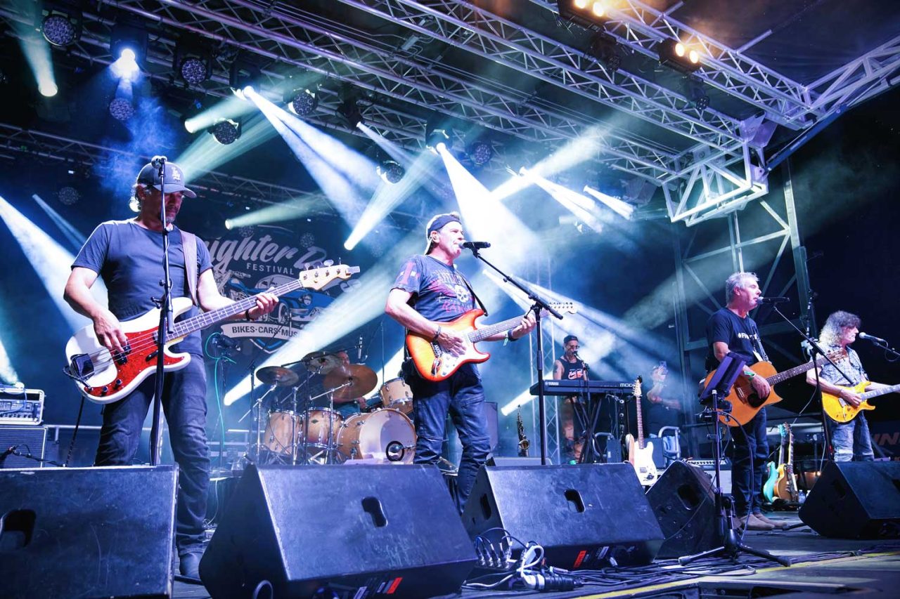 Band performing beneath crossing white beams at the 2024 Brighter Days festival.