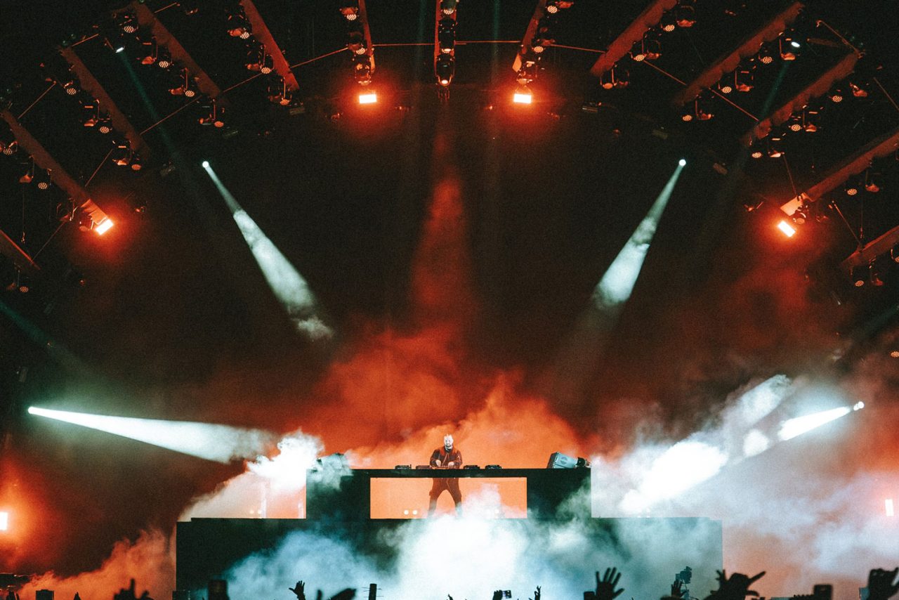 DJ performing amid red lighting, white beams and stage haze at Coachella 2024.