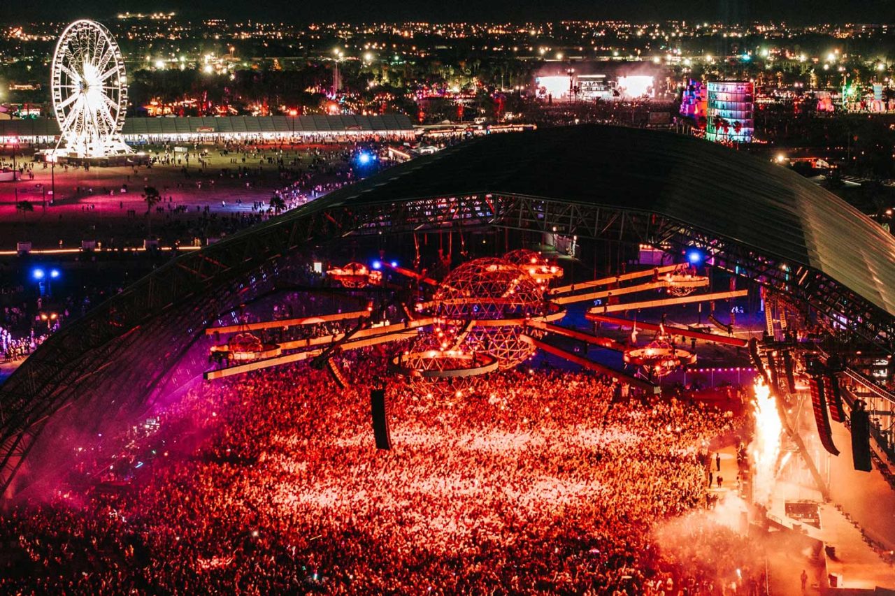 Aerial night view of a large Coachella crowd under red stage lighting.