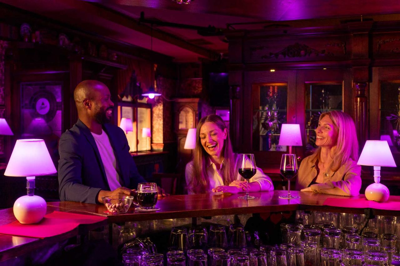 Three people at a bar lit by colourful table lamps using Astera LunaBulb.
