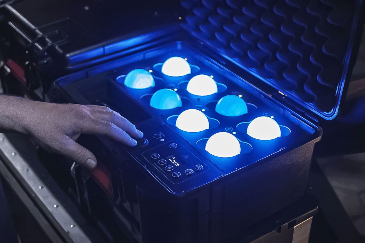 Hand adjusting controls beside glowing LunaBulbs in a carrying case.