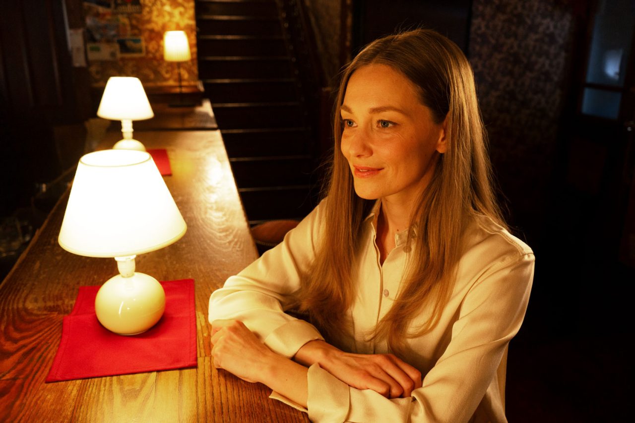Woman seated beside a table lamp casting warm light across her face.