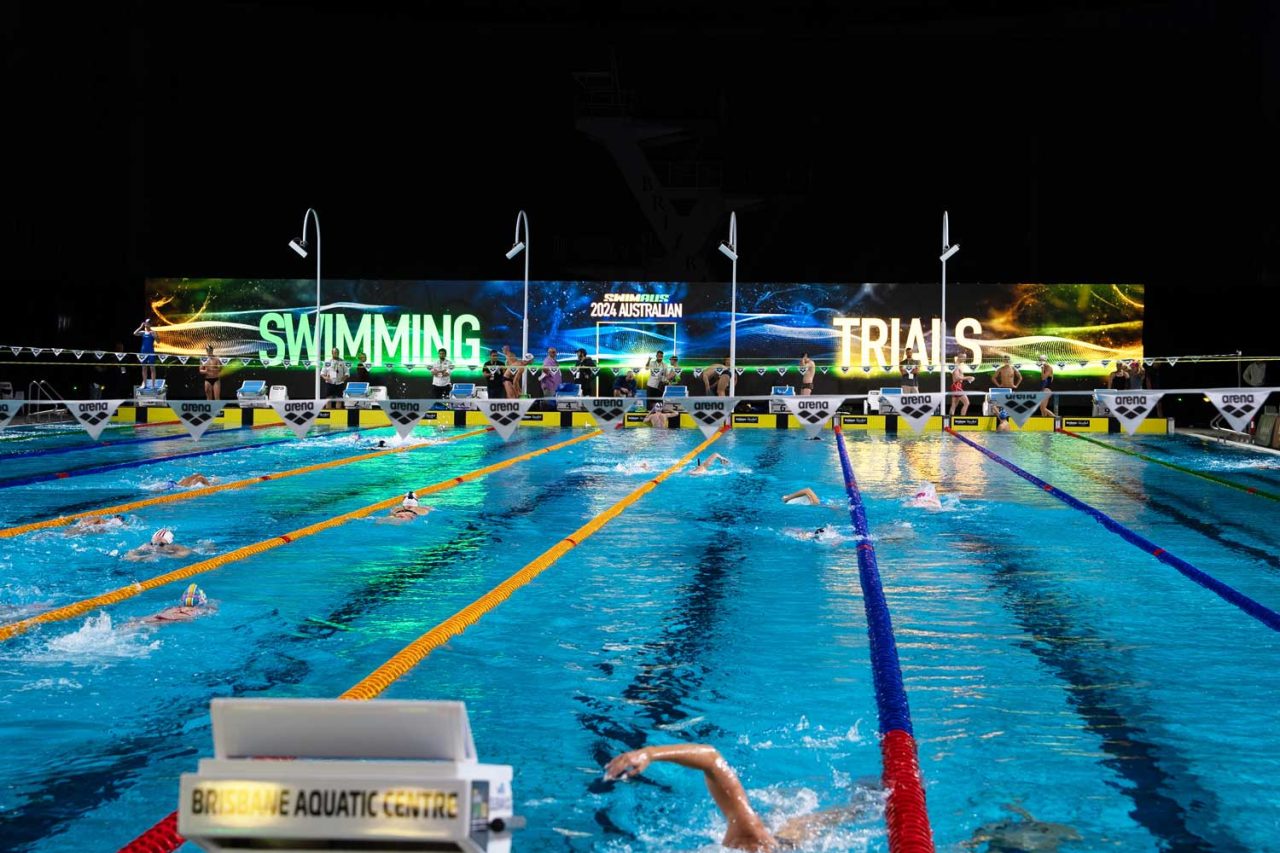 View along the pool lanes towards the illuminated Swimming Trials backdrop in 2024.