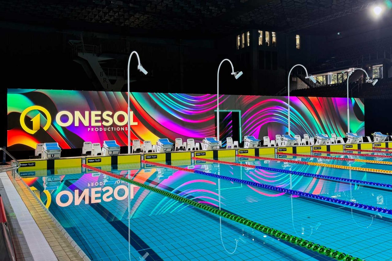 Onesol branding and colourful patterns on the LED backdrop behind the pool starting blocks.