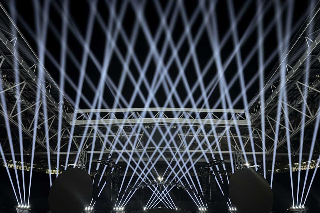 Dense array of crossing white beams above a concert lighting rig.