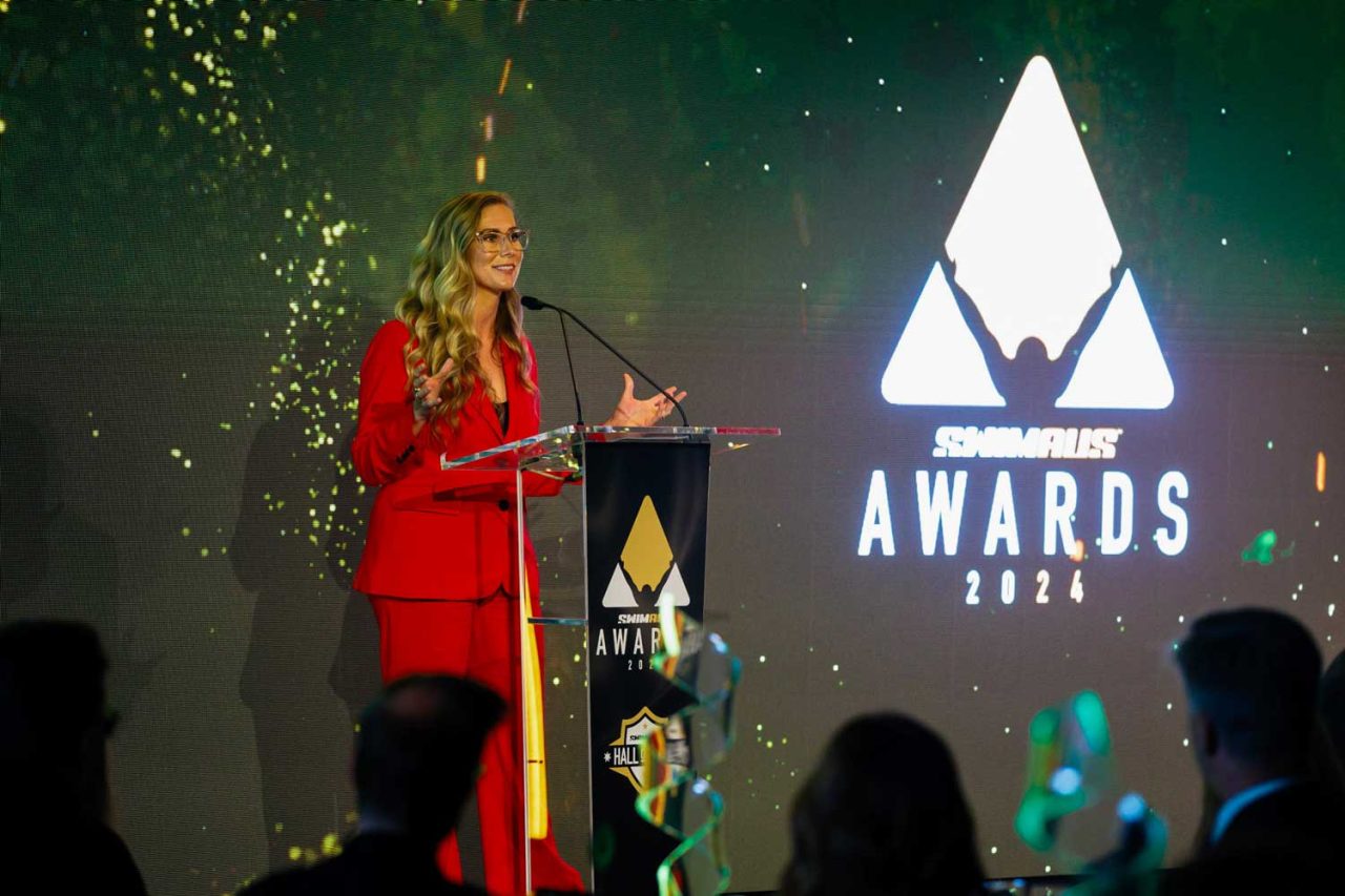 A speaker at the podium in front of the 2024 SwimAus Awards screen.