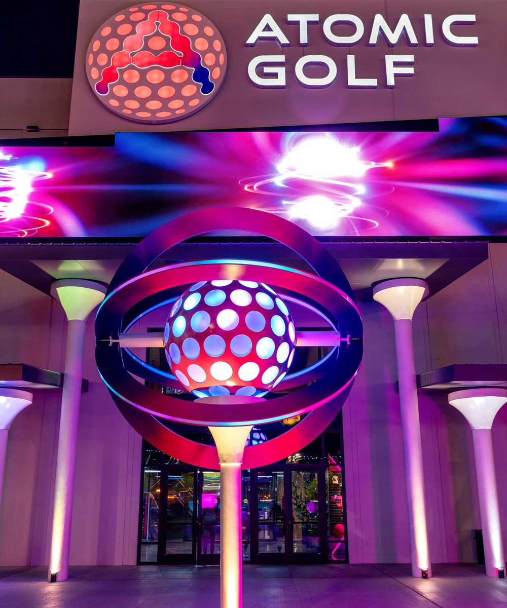 Colourful circular lighting fixture beneath an Atomic Golf sign.