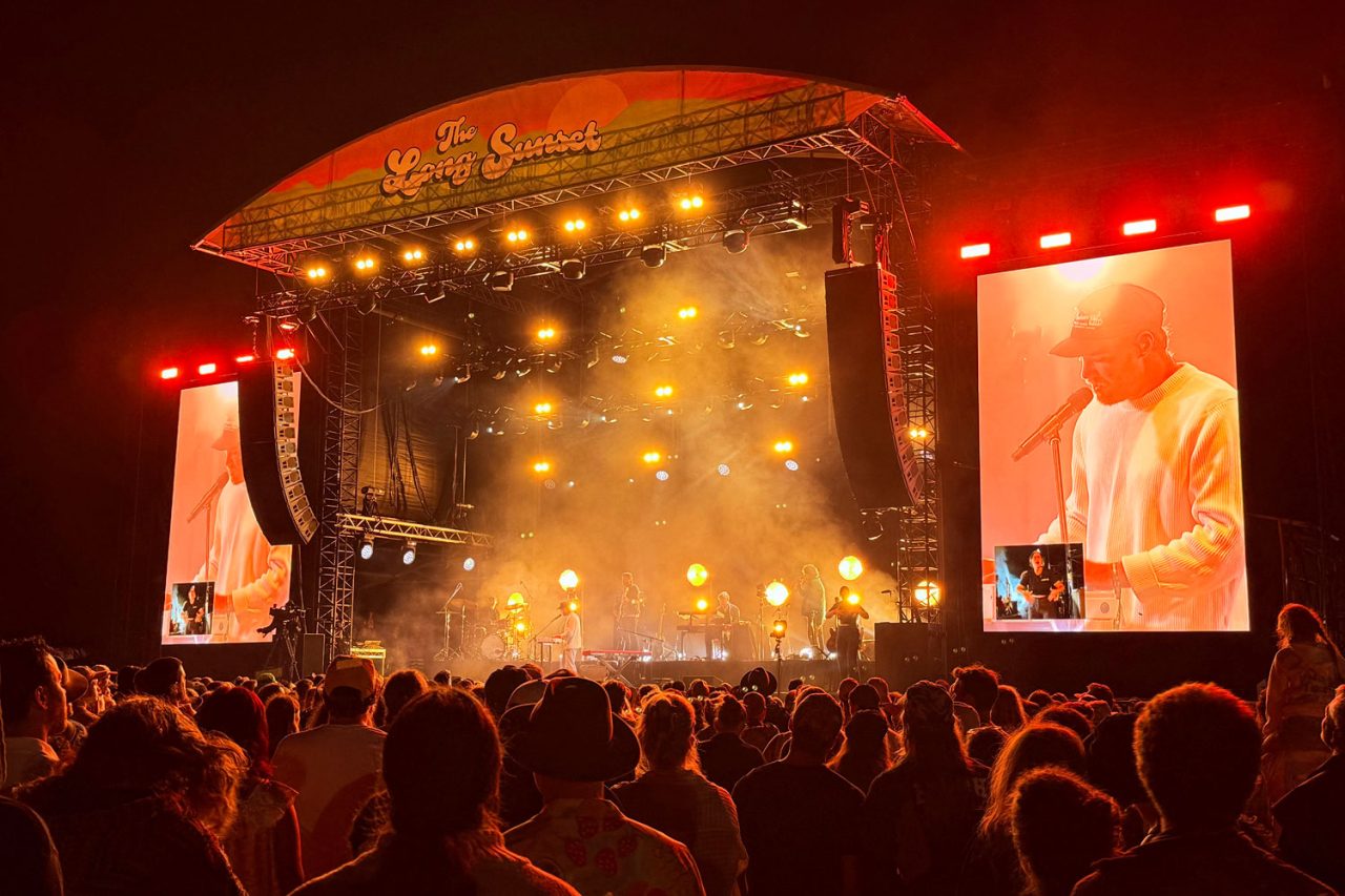 Amber stage lights above the crowd and side screens at The Long Sunset.