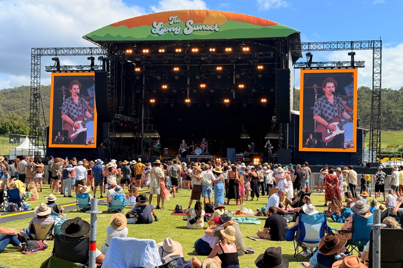Daytime crowd on the lawn facing The Long Sunset stage and side screens.