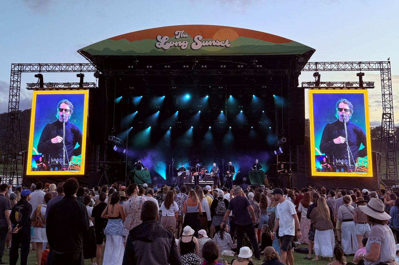 Festivalgoers face the stage and live video screens at The Long Sunset in the evening.