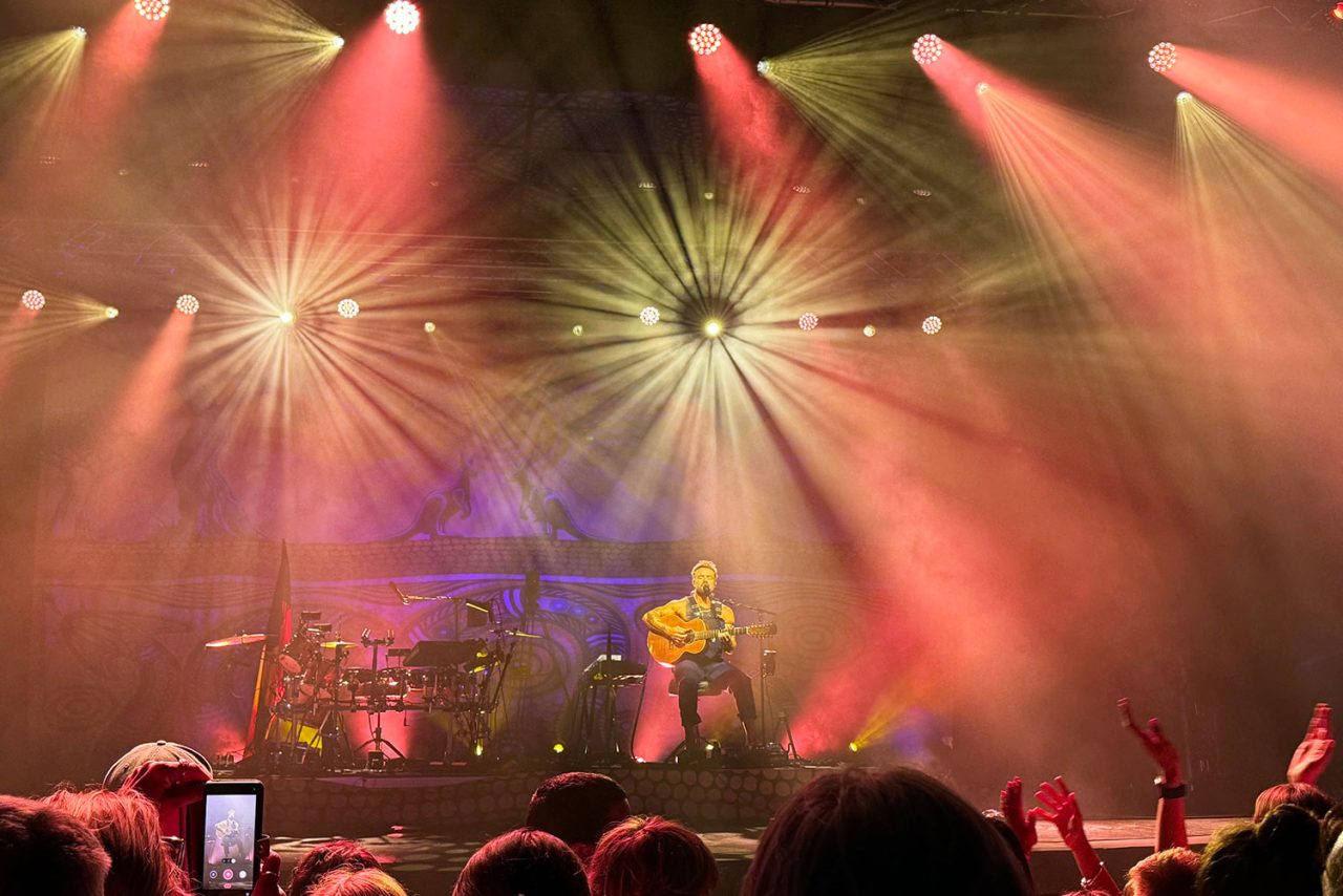 Red wash lighting and gold beams surround the performer during the Freedom Sessions show.