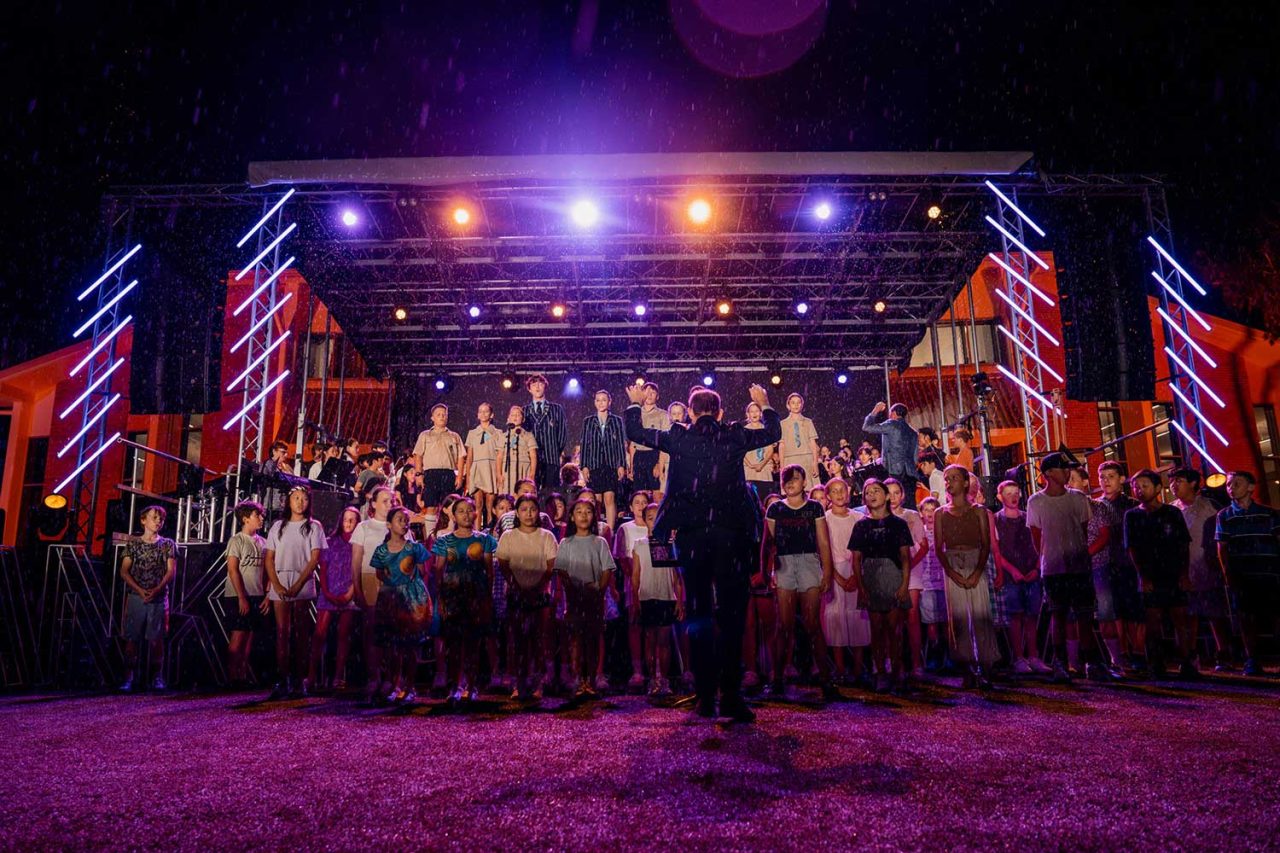 Choir across the stage beneath coloured lighting at All Saints Anglican School's farewell celebration.