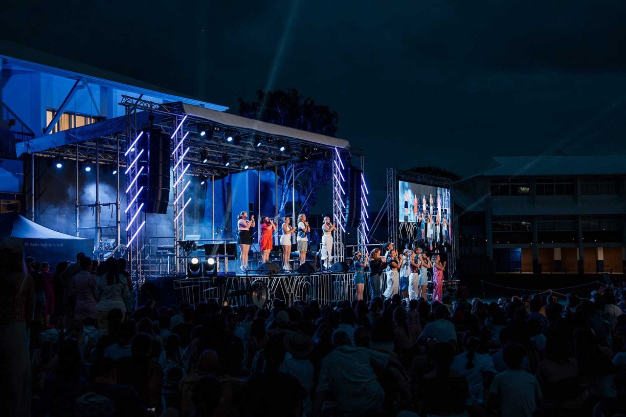 Nighttime audience facing the stage and large screen at All Saints Anglican School.