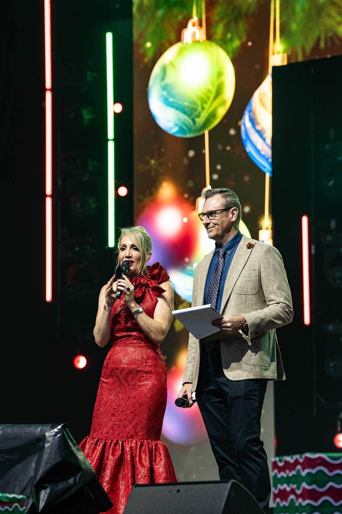 Two presenters beside festive video imagery at the 2024 Gold Coast Mayor's Carols.