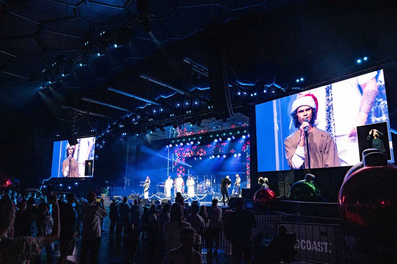 Singer shown on a large side screen beside the carols stage.