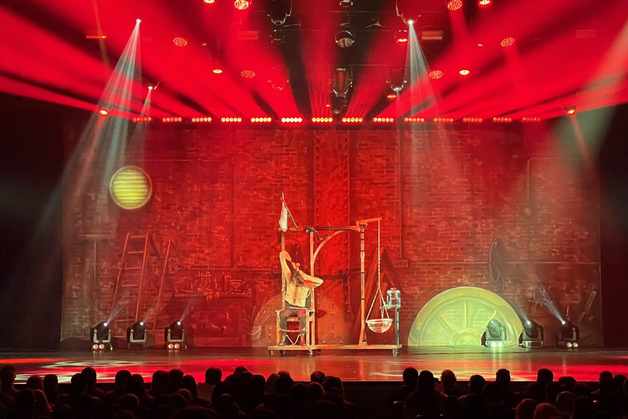 Wide view of the illusion set beneath red beams during the Decennium show.