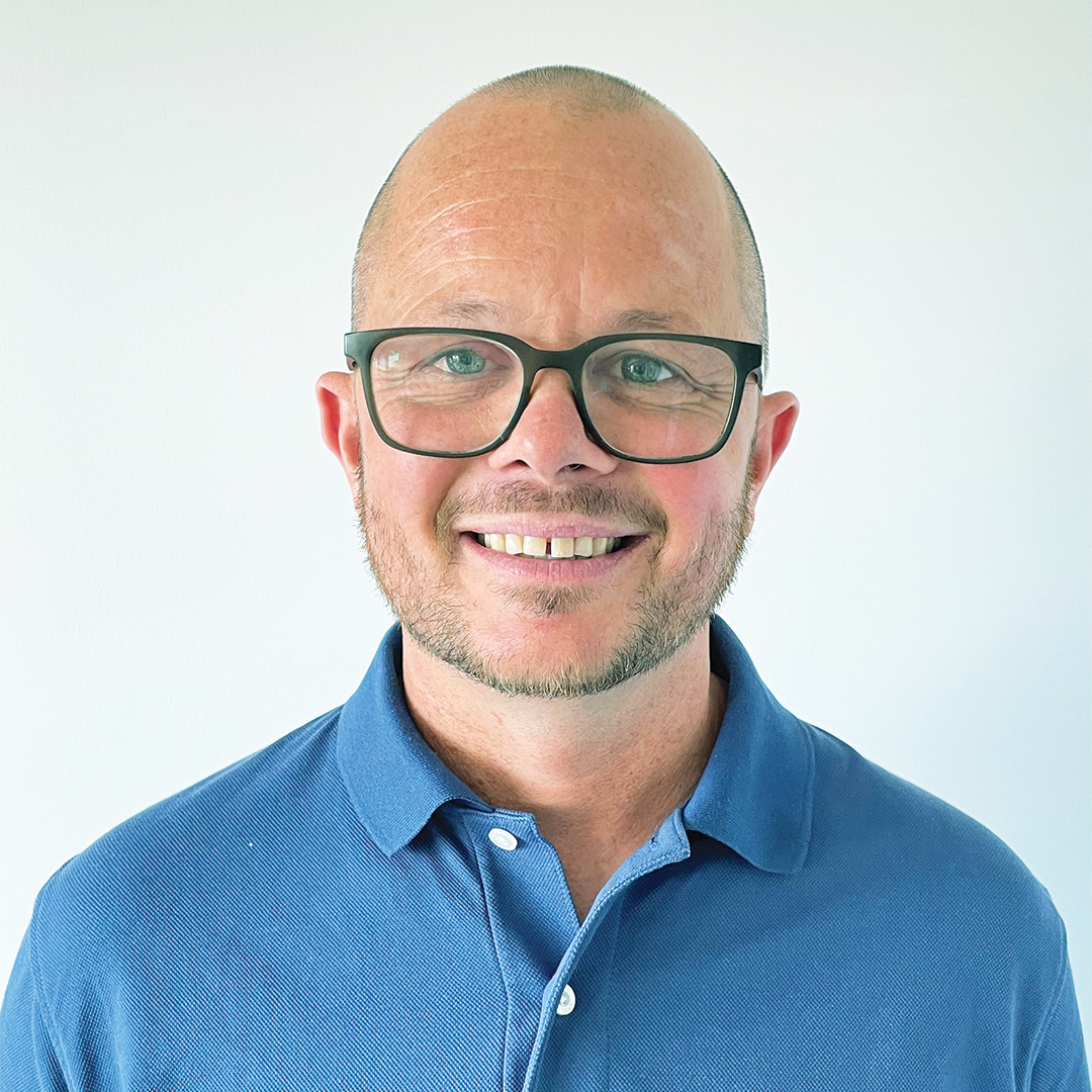 Portrait of Mike wearing glasses and a blue shirt.