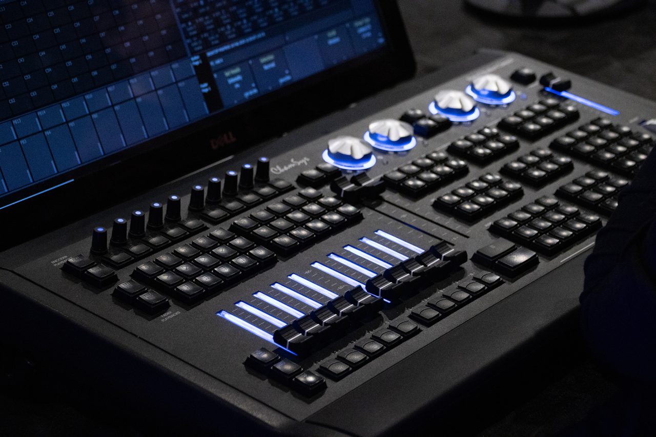 Close view of a ChamSys console with illuminated faders and rotary controls.