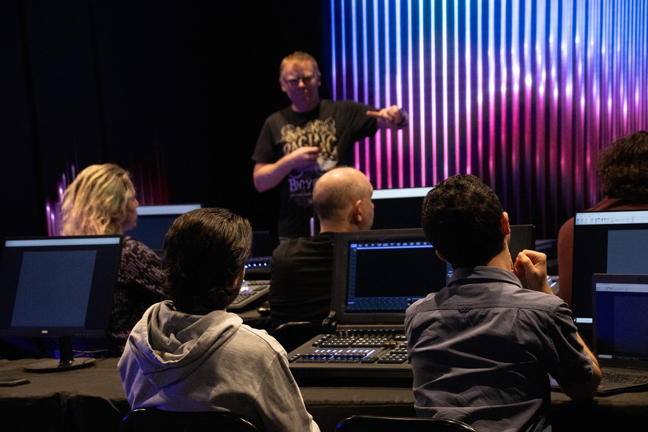 Participants listening to a trainer beside a colourful LED display.