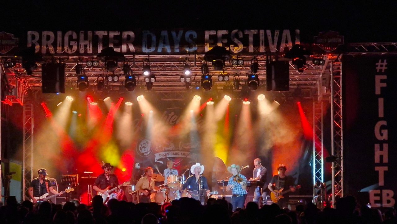 Band on the Brighter Days Festival stage beneath warm white, red and yellow beams.