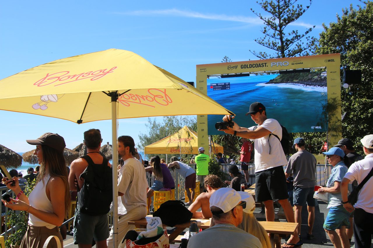 Visitors watch a surf screen beneath yellow umbrellas at the Gold Coast Pro.