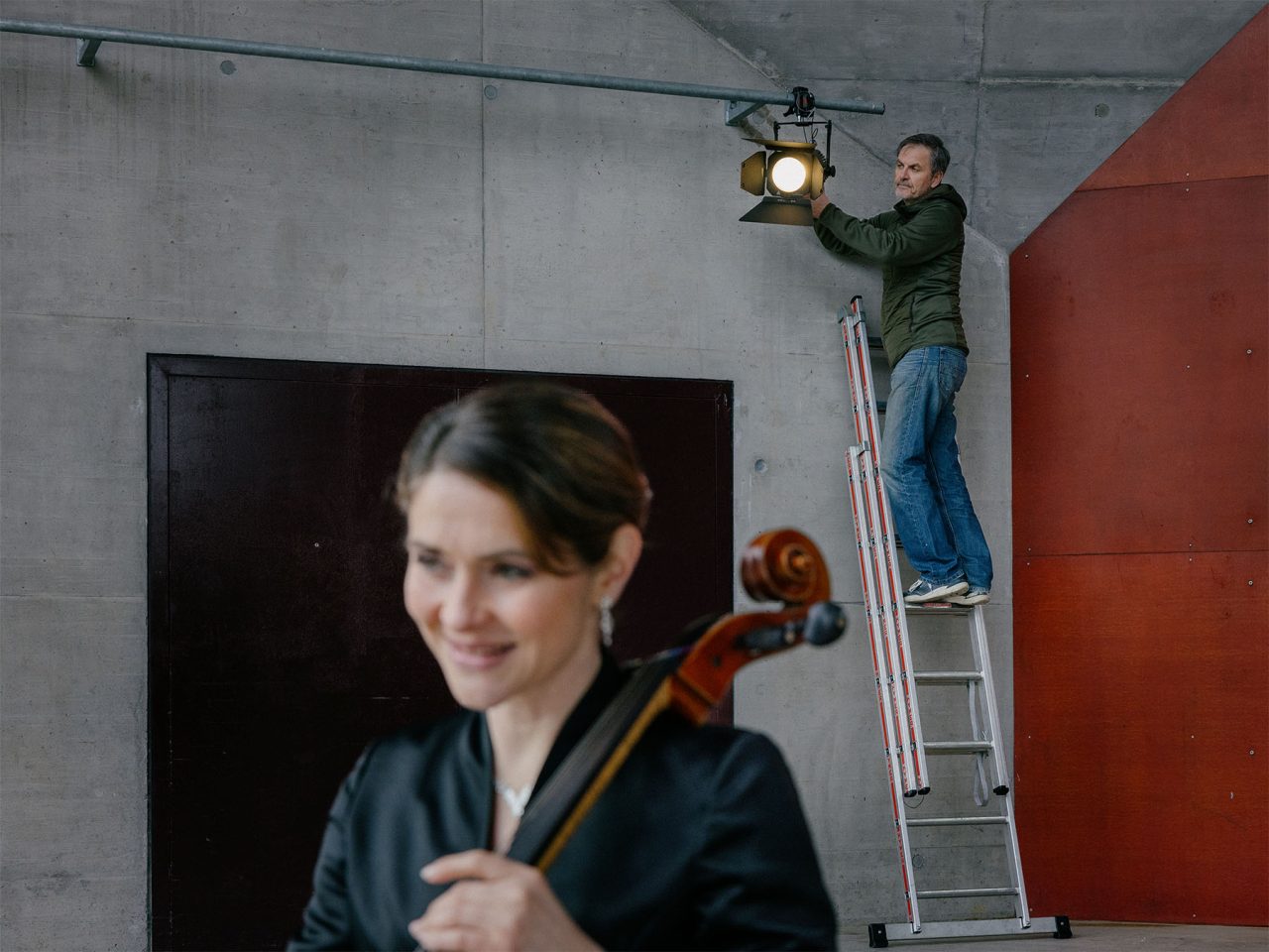 Crew member on a ladder adjusting a QuikPunch above a seated cellist.