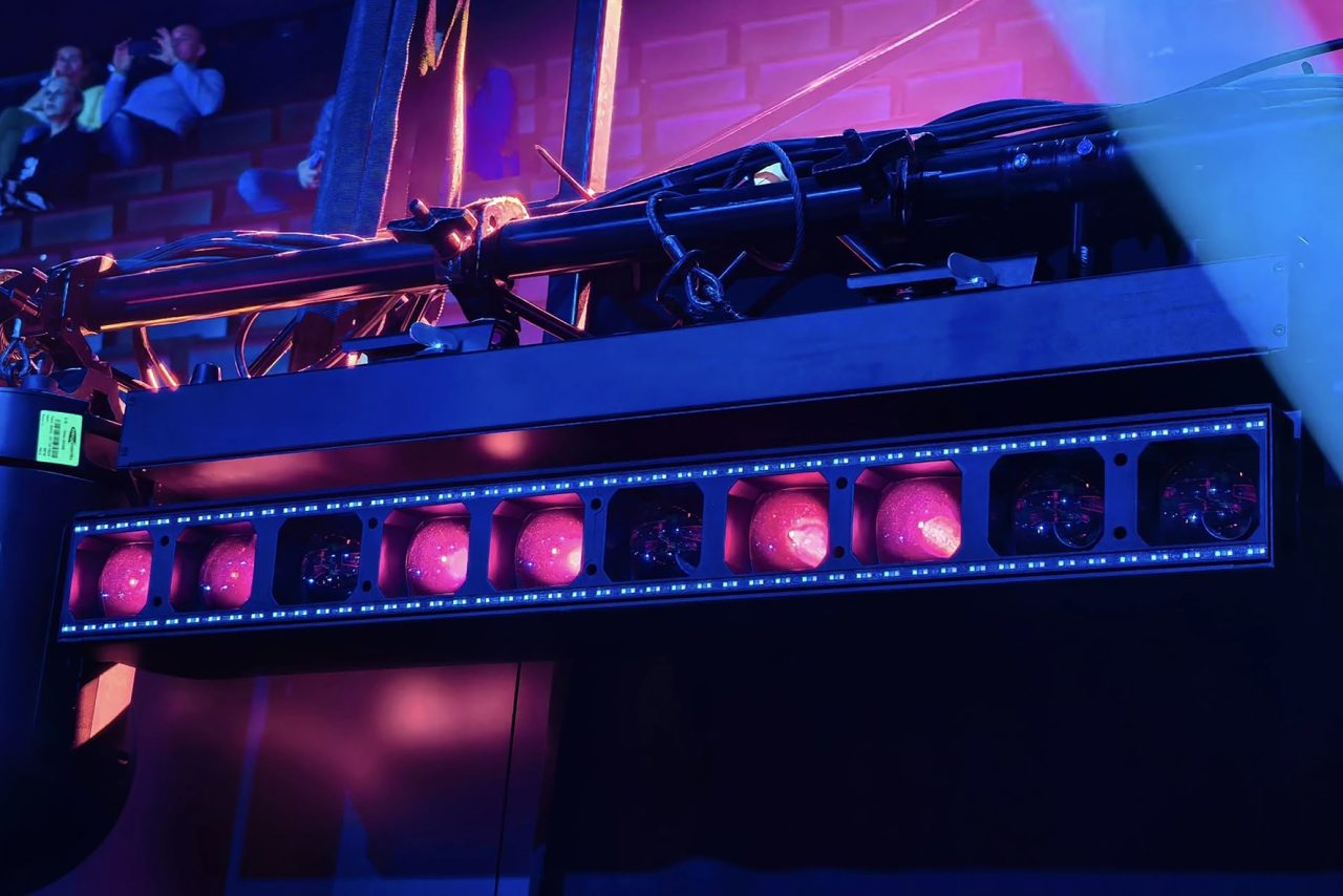 Close view of rigged lighting fixtures with pink and blue illuminated lenses.