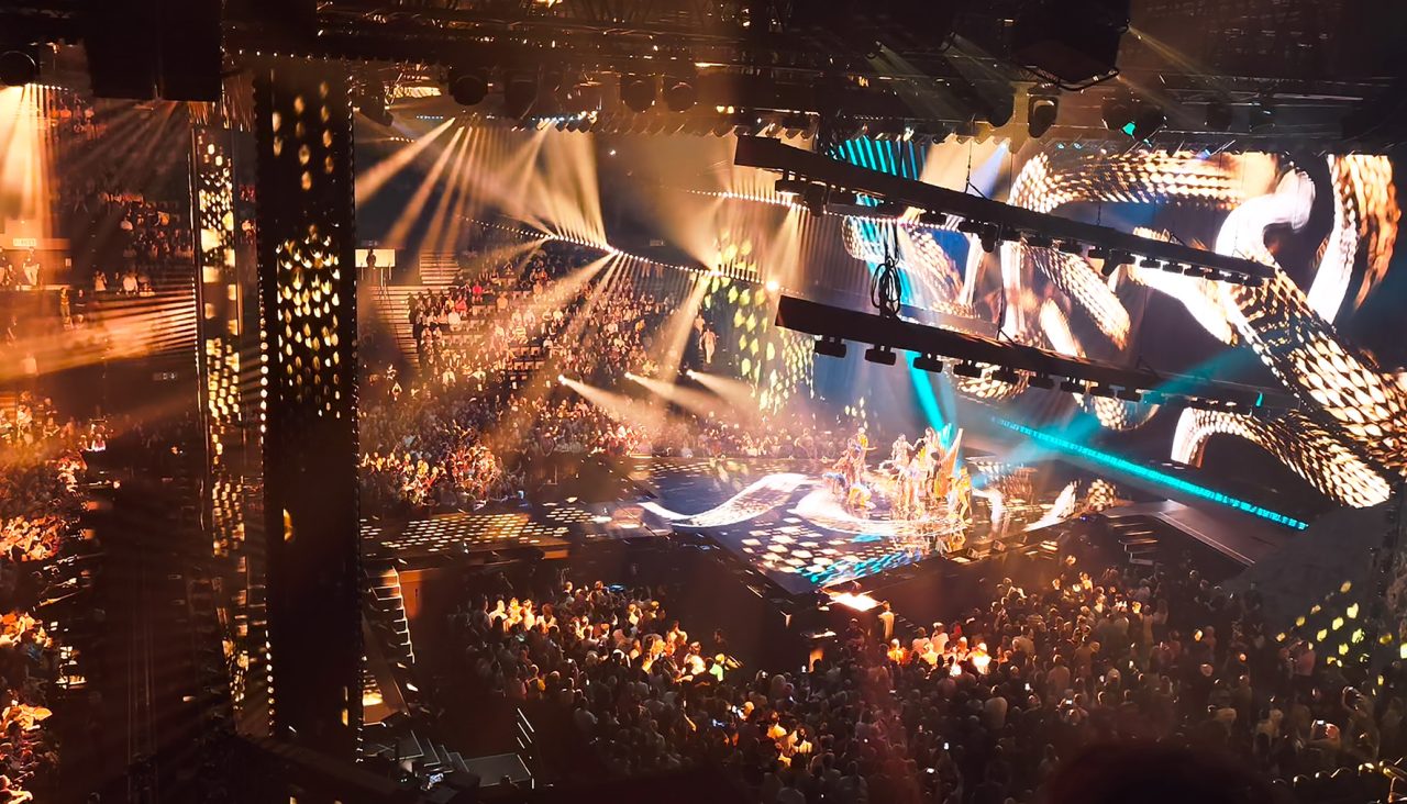Elevated view of the Eurovision arena glowing gold around the stage.