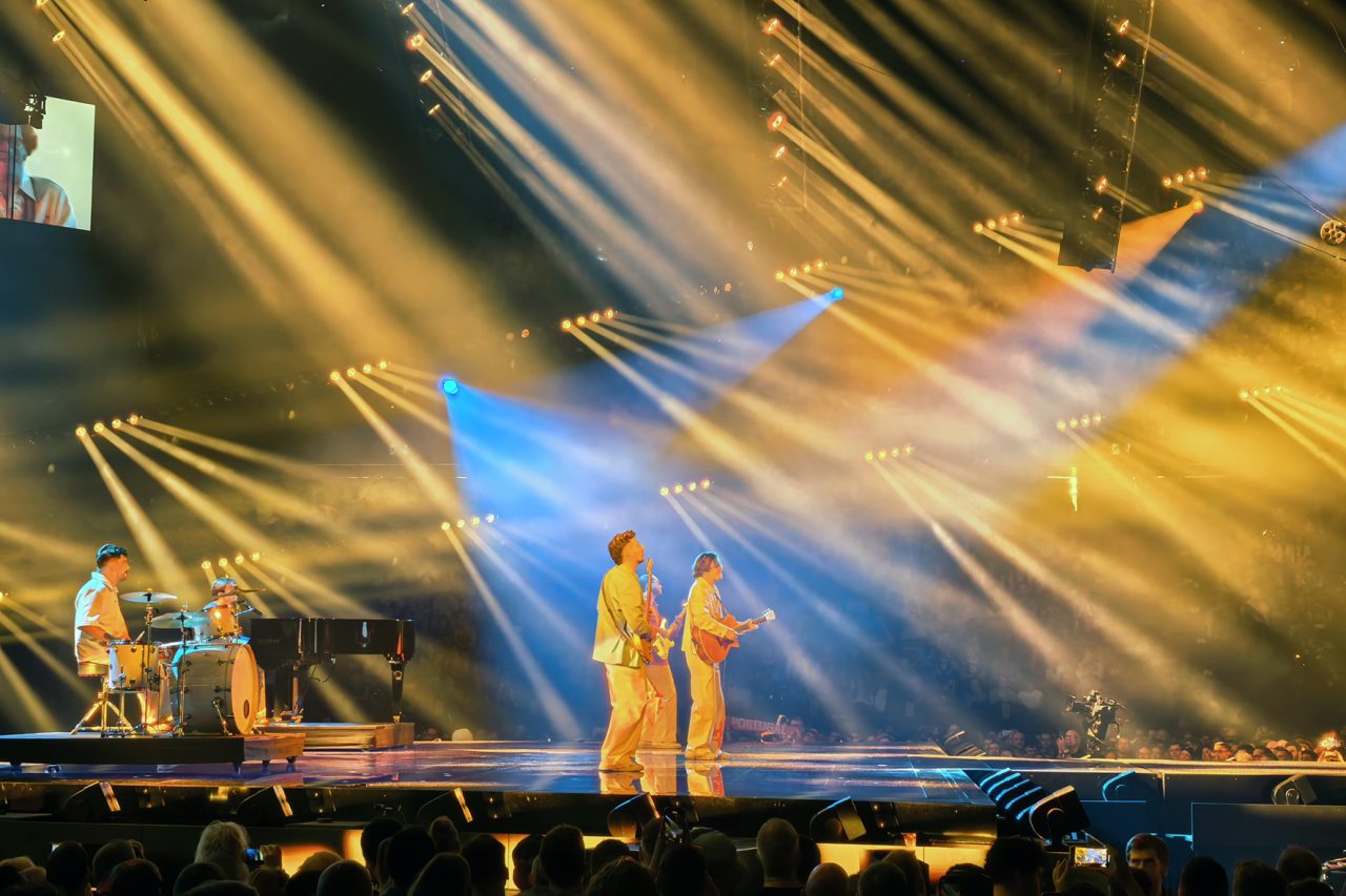 Performers beneath sweeping gold and blue beams on the Eurovision stage.