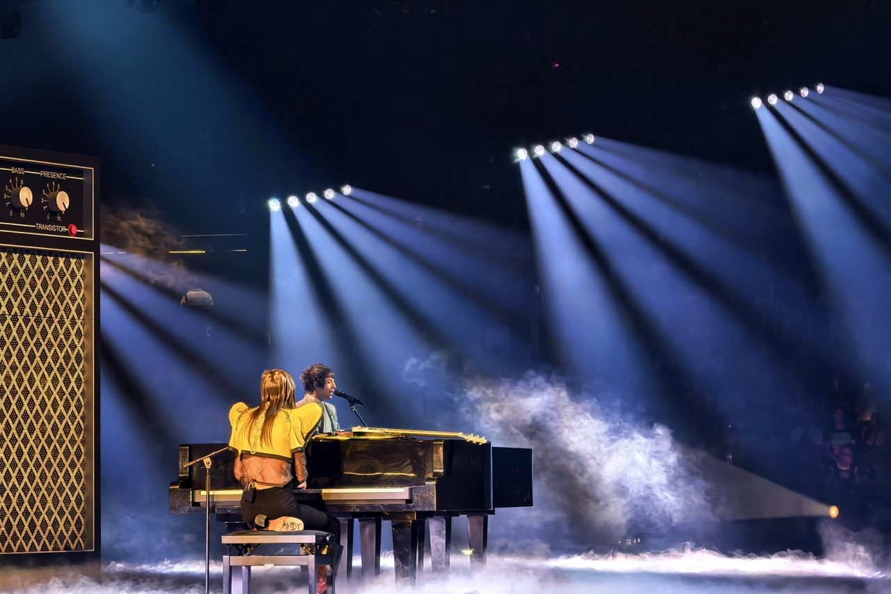 Piano performance beneath blue-white spotlights and stage haze at Eurovision 2025.