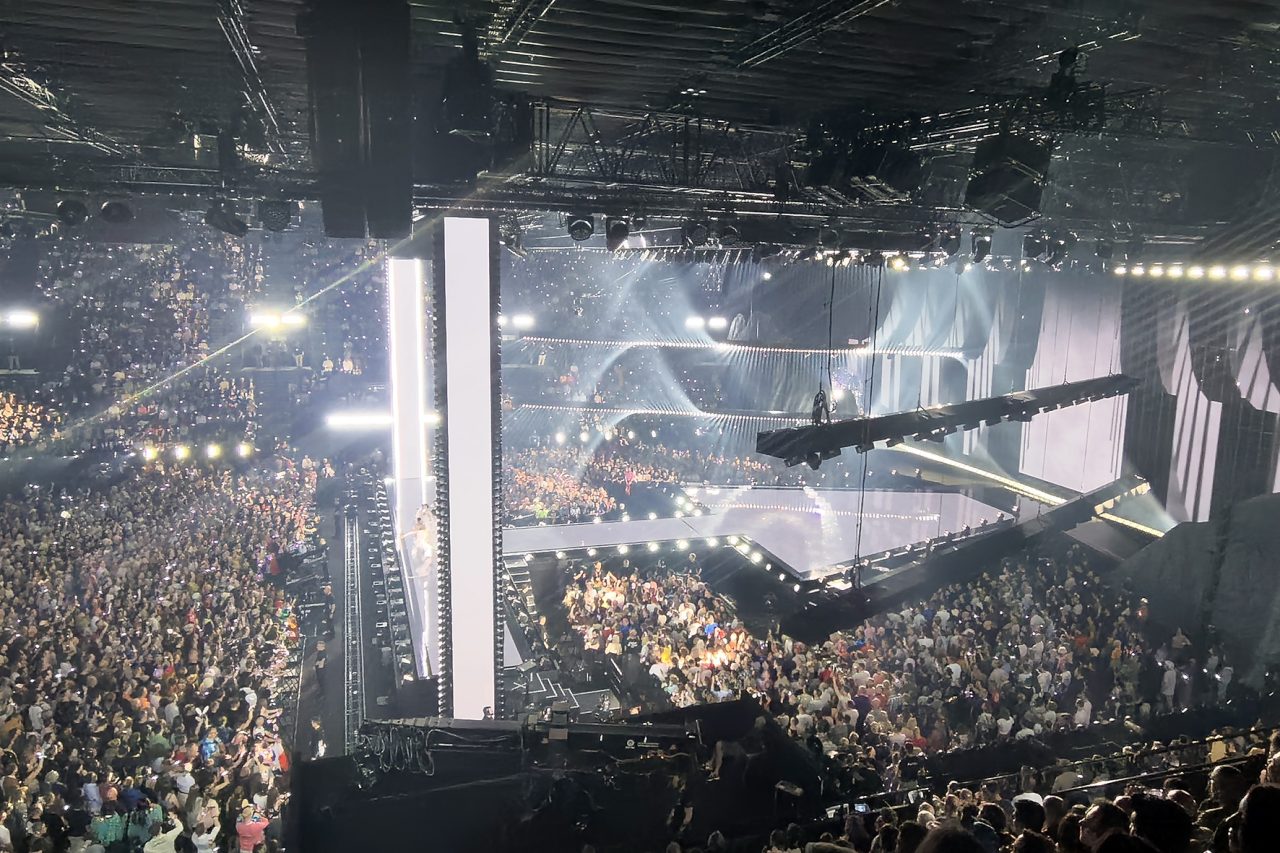 Bright white lighting illuminating the Eurovision stage and packed arena.