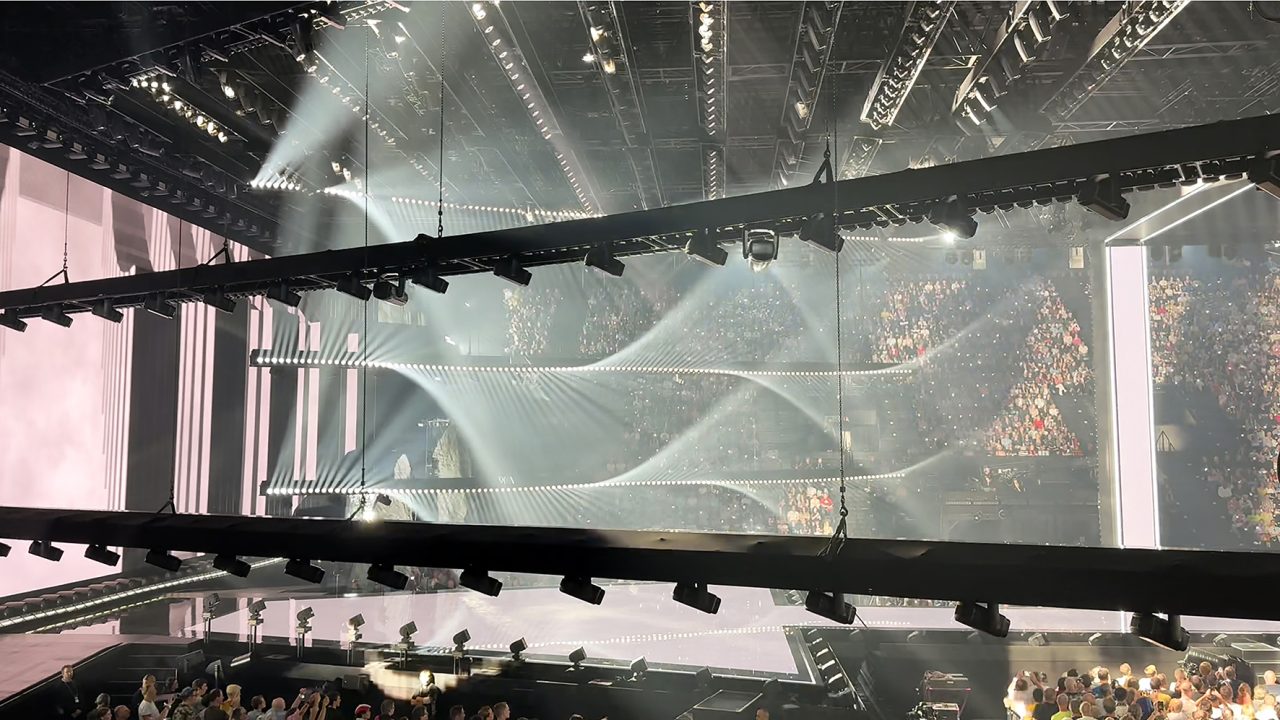 Layered lighting trusses in front of white wave graphics on the Eurovision stage.